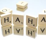 Een aantal scrabbelstenen. Vier staan er achter elkaar en vormen het woord "haha".